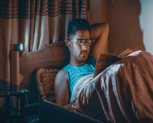 Person reading a book in bed at night illuminated only by a small warm reading lamp
